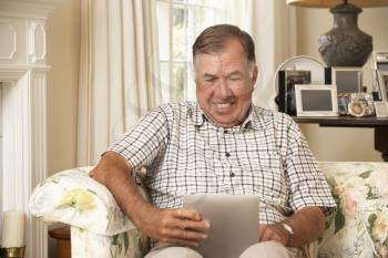 Retired Senior Man Sitting On Sofa At Home Using Tablet Computer