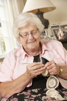 Retired Senior Woman Sitting On Sofa At Home Doing Crochet