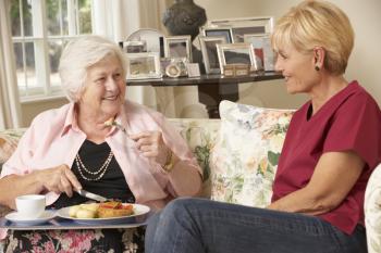 Helper Serving Senior Woman With Meal In Care Home