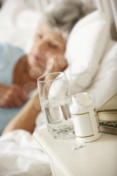 Medication On Bedside Table Of Sleeping Senior Woman