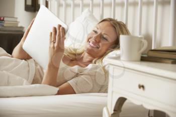Woman Using Digital Tablet In Bed At Home