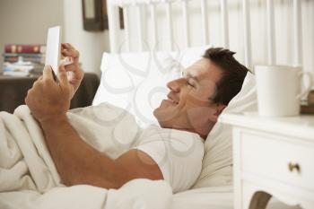 Man Using Digital Tablet In Bed At Home