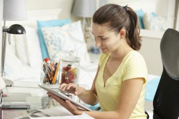 Teenage Girl Studying At Desk In Bedroom Using Digital Tablet
