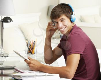 Teenage Boy Studying At Desk In Bedroom Using Digital Tablet
