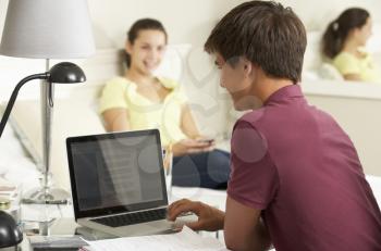 Teenage Boy Studying At Desk In Bedroom With Girl In Background