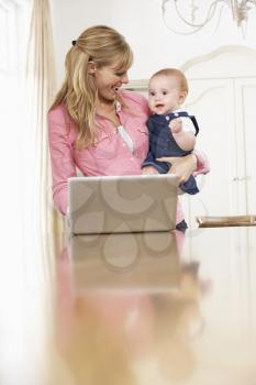 Mother Holding Baby Daughter Whilst Using Laptop