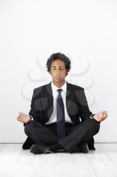 Studio Portrait Of Businessman Sitting On Floor Meditating