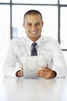Businessman Sitting At Desk In Office Using Digital Tablet