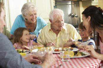 Multi Generation Family Eating Meal Together In Kitchen