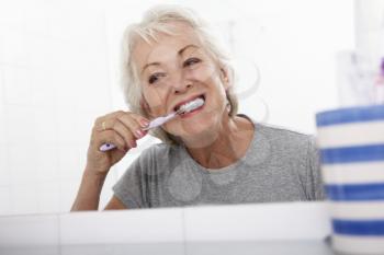 Senior Woman In Bathroom Brushing Teeth