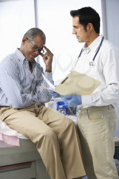 Doctor In Surgery With Male Patient Reading Notes