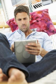 Man Relaxing In Garden Hammock Using Digital Tablet