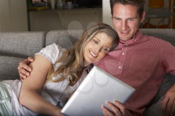 Couple Sitting On Sofa Looking At Digital Tablet