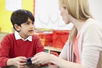 Teacher Helping Male Pupil With Maths At Desk