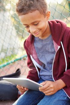 Young Boy Using Digital Tablet Sitting In Park