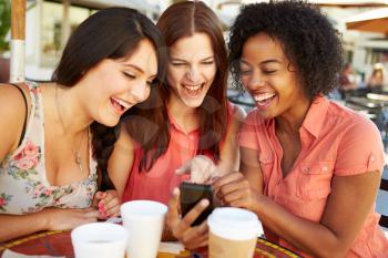 Three Female Friends Reading Text Message In Caf