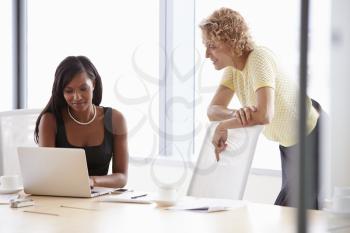 Two Businesswomen Working Together On Laptop In Boardroom