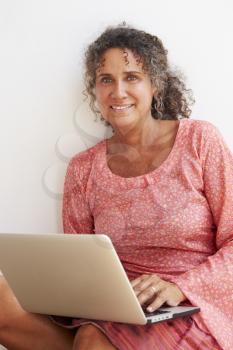 Mature Woman Sitting Against Wall Using Laptop