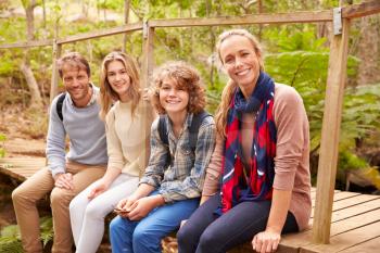 Portrait of family sitting on a bridge in a forest, side view
