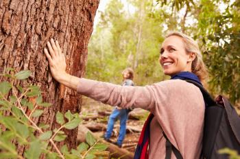 Woman touching a tree in a forest, her son in the background