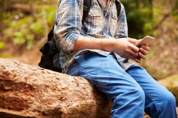 Boy sitting in a forest using a smartphone, close up