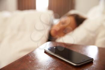 Woman Asleep In Bed With Mobile Phone On Bedside Table