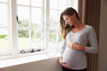 Pregnant Woman Standing By Window Holding Belly