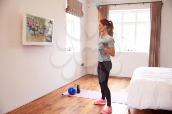Woman Working Out To Fitness DVD On TV In Bedroom