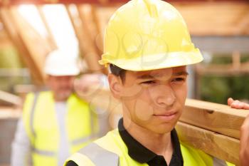 Builder And Apprentice Carrying Wood On Construction Site