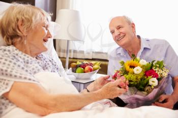 Husband Visiting Senior Wife In Hospital With Flowers