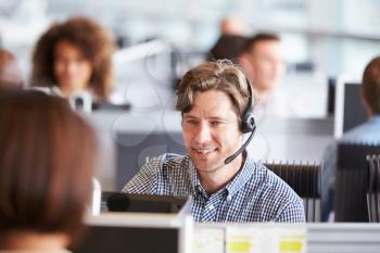 Young man working in call centre, surrounded by colleagues