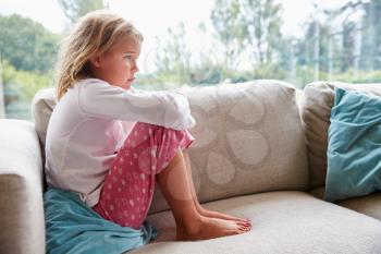 Unhappy Young Girl Sitting On Sofa At Home