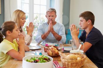 Family Saying Prayer Before Enjoying Meal At Home Together