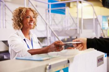 Staff At Airport Check In Desk Handing Ticket To Passenger