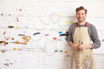 Portrait Of Male Artist Leaning Against Paint Covered Wall