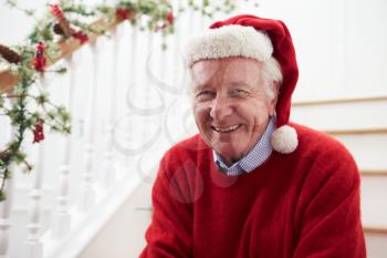 Grandfather Wearing Santa Hat Sitting On Stairs At Christmas