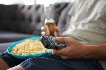 Man Sitting On Sofa Holding TV Remote And Bottle Of Beer