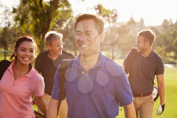 Group Of Golfers Walking Along Fairway Carrying Golf Bags