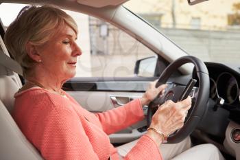 In car view of senior female driver using smartphone