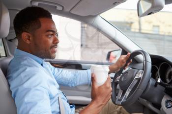 Young African American male driver with coffee, in car view