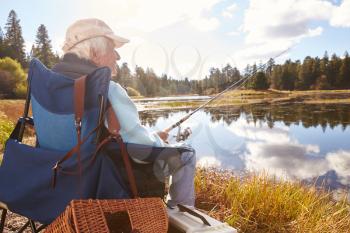 Senior man sits fishing in a lake, back view close-up