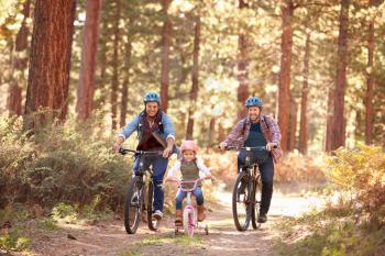Gay Male Couple With Daughter Cycling Through Fall Woodland