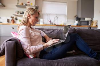 Woman Relaxing On Sofa Using Laptop In Modern Apartment