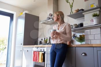 Woman Standing In Kitchen With Hot Drink