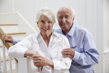 Portrait Of Senior Couple Standing By Staircase At Home