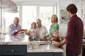 Family With Grandparents Make Roast Turkey Meal In Kitchen