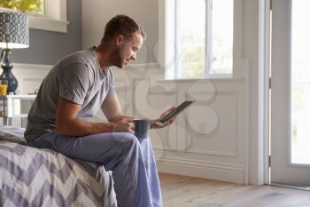 Man Wearing Pajamas Using Digital Tablet In Bedroom