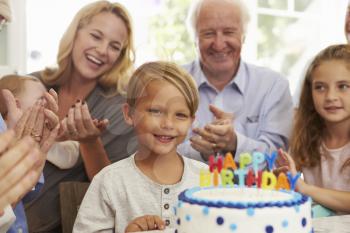 Boy Blows Out Birthday Cake Candles At Family Party