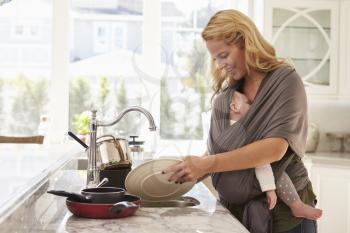 Busy Mother With Baby In Sling Multitasking At Home