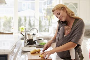 Busy Mother With Baby In Sling Multitasking At Home